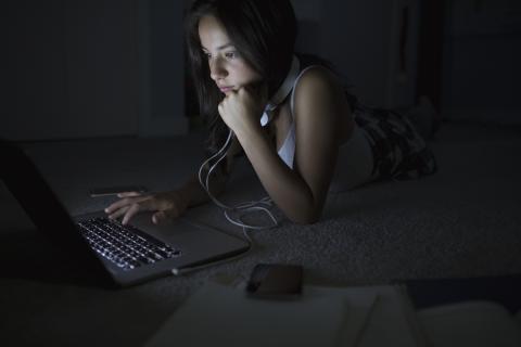 A teenager sitting in the dark using a laptop