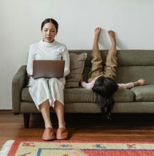 A mother works on a laptop with her child beside her