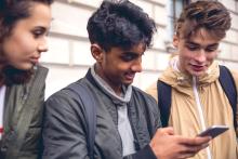 A group of teens looking at a cellphone and smiling