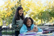 Two girls smiling while looking at a cell phone.